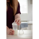Nuk Simply Natural 5 oz bottle held by a hand, with a slow flow nipple, next to a transparent lid on a wooden surface.