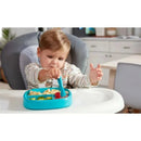 A young child using a blue Nuk pretensil dipper spoon to eat food from a divided plate on a high chair.