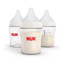 Three Nuk 5 oz baby bottles with white nipples, one transparent, and two with cream-colored contents and measurement markings.