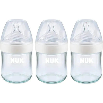 Three NUK Simply Natural glass baby bottles, 4 oz, with clear glass bodies and white caps featuring nipple tops.