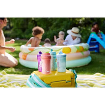 Four Nuk Advanced Hard Spout Spill Proof Sippy Cups in pastel colors on a yellow cooler, with children playing in a pool nearby.