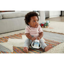 A baby sits on a colorful rug, holding a Nuk Glow-In-The-Dark 5 Oz Learner Cup, looking happy and engaged.