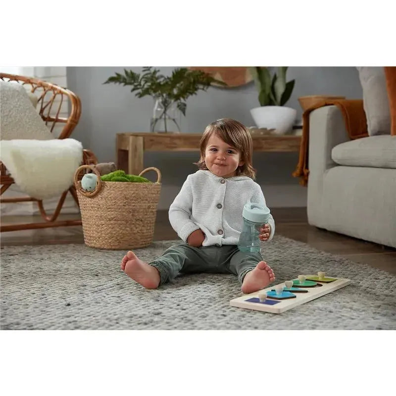 A toddler sits on a rug, smiling while holding a NUK Nature Everlast Weighted Straw Cup, with a colorful shape sorter next to them.