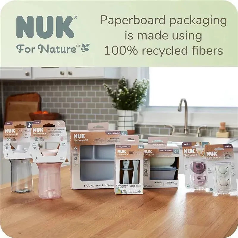 Weighted straw cups and other NUK products displayed on a wooden kitchen counter, with eco-friendly packaging information visible.
