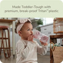 Toddler drinking from a NUK weighted straw cup made of break-proof Tritan plastic, wearing a headband and a cozy sweater.