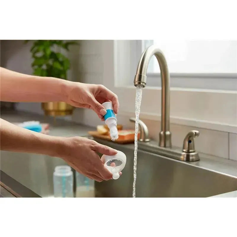 Nuk Smooth Flow Pro Anti-Colic Baby Bottle being cleaned under running water, with a bottle brush in hand.