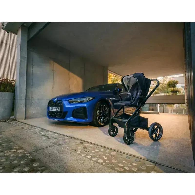 Nuna MIXX™ next Stroller with Magnetic Buckle in black, positioned beside a blue BMW in a modern garage setting.