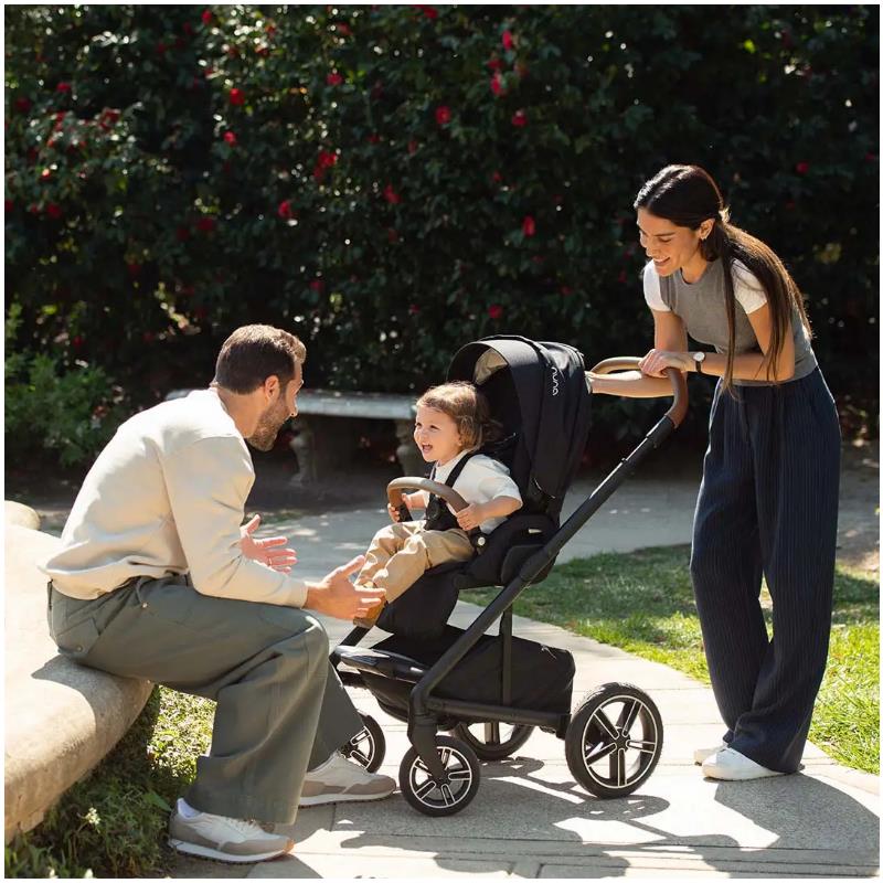 Nuna MIXX™ next stroller in Sterling color, with a smiling child seated, while a man interacts animatedly and a woman observes.