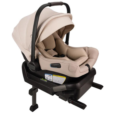 Nuna PIPA™ aire Infant Car Seat in Biscotti color, securely attached to the PIPA™ Series Base, featuring a protective canopy and safety labels.