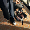 Nuna PIPA™ aire Infant Car Seat in black with a baby inside, held by an adult on a tiled floor.
