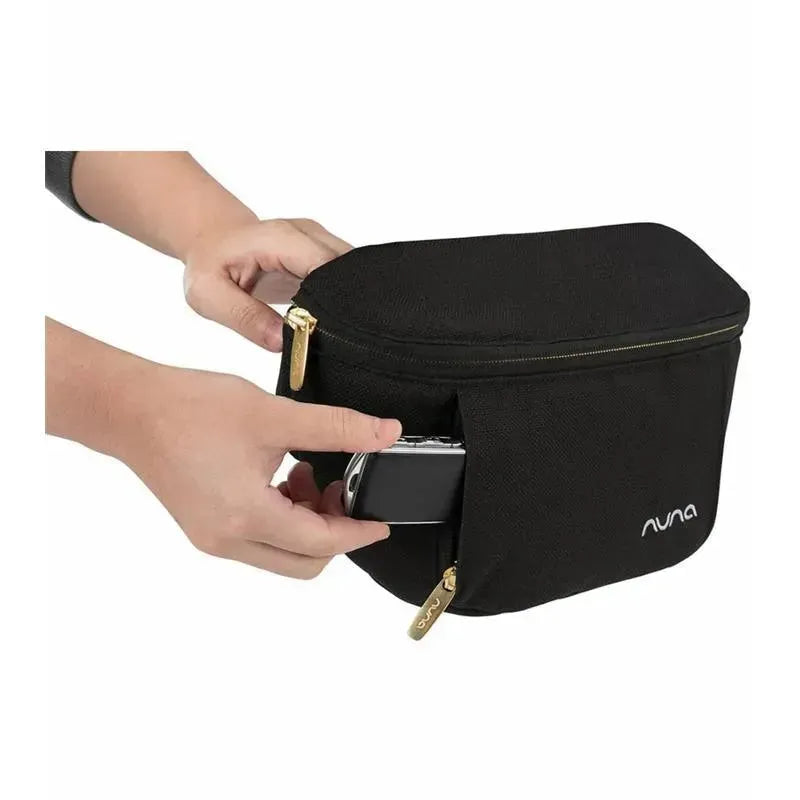 Nuna Stroller Sling Bag in black, person inserting a phone into the front pocket, visible gold zippers and logo.