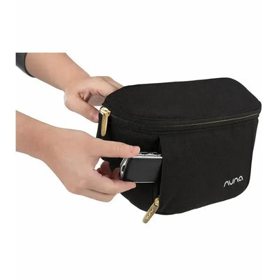 Nuna Stroller Sling Bag in black, person inserting a phone into the front pocket, visible gold zippers and logo.