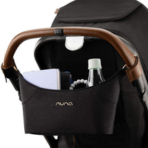 Stroller organizer featuring a black fabric design with leather handle, holding a water bottle, notebook, and teething beads.