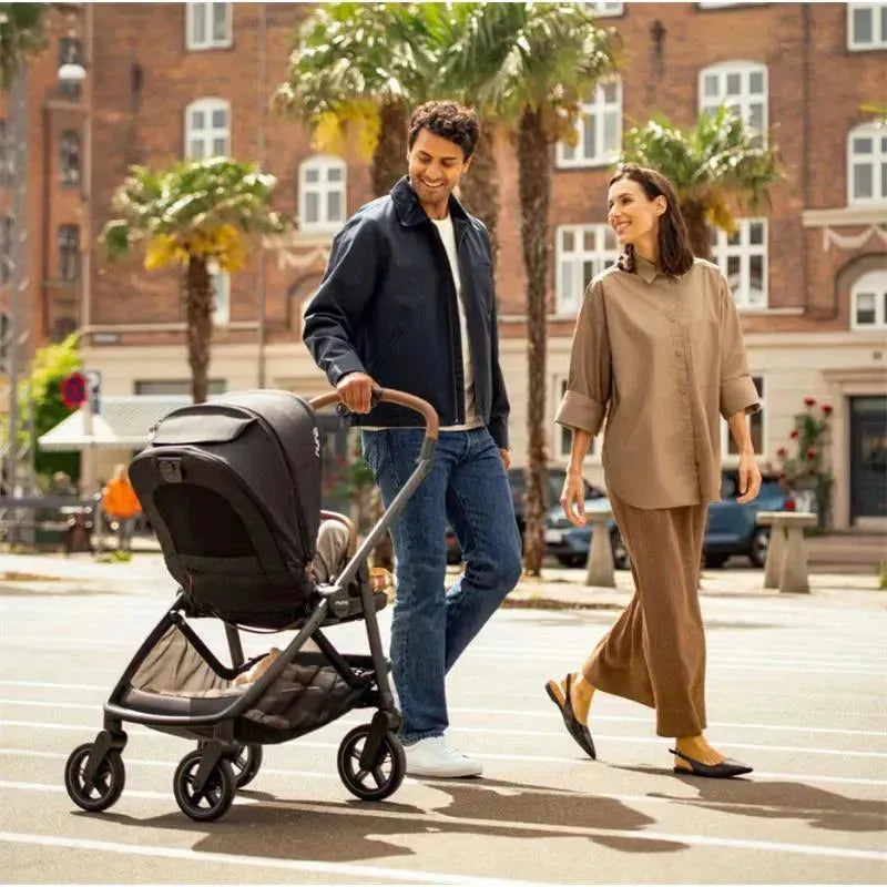 Couple walking outdoors with Nuna SWIV™ stroller in Biscotti color, featuring a sleek, modern design and spacious seat.