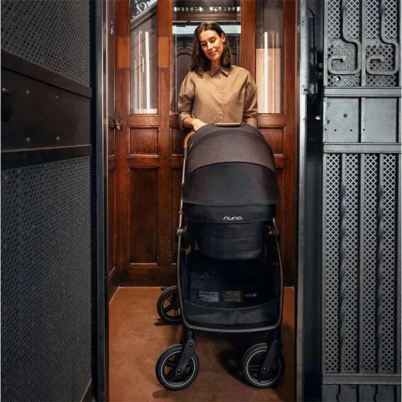 Nuna SWIV™ stroller in Biscotti color, with a woman in an elevator, showcasing its sleek design and portability.
