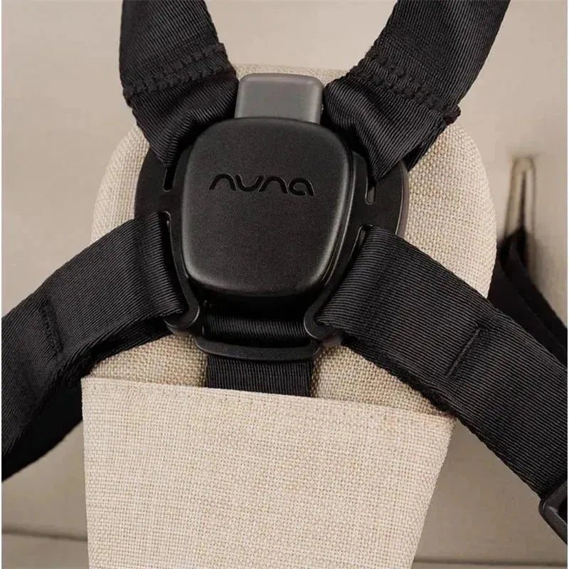 Black harness buckle with Nuna logo on a soft tan fabric background, designed for secure stroller use.