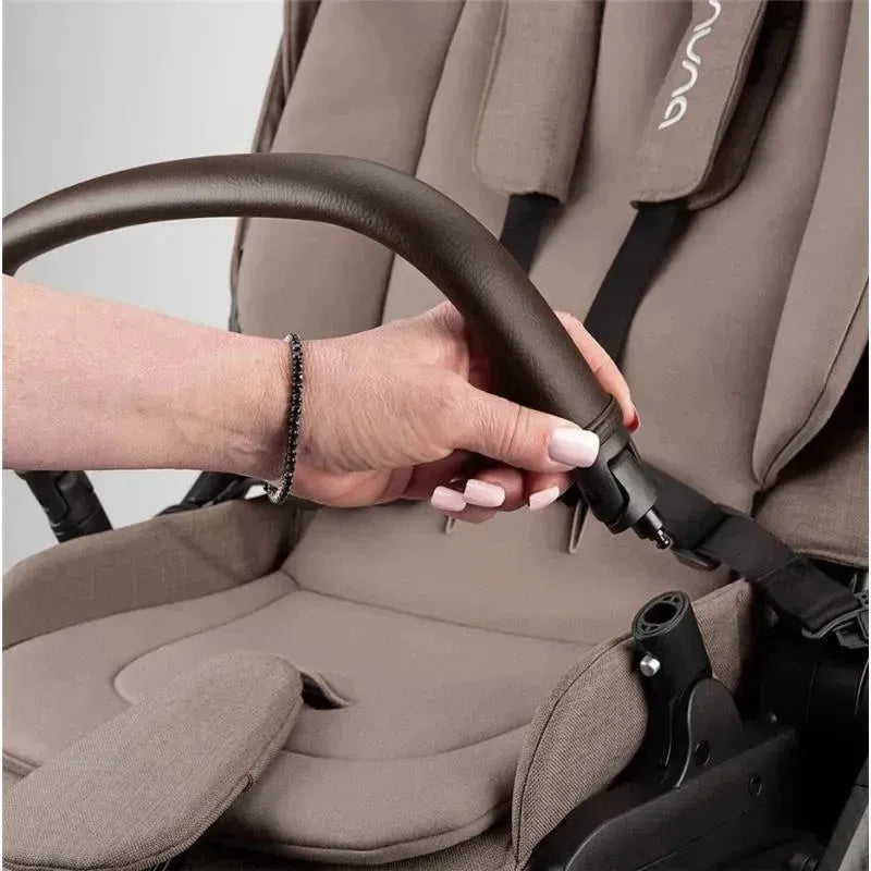 A hand adjusts the brown handle of the Nuna SWIV™ Stroller, showcasing its sleek design and padded seating.