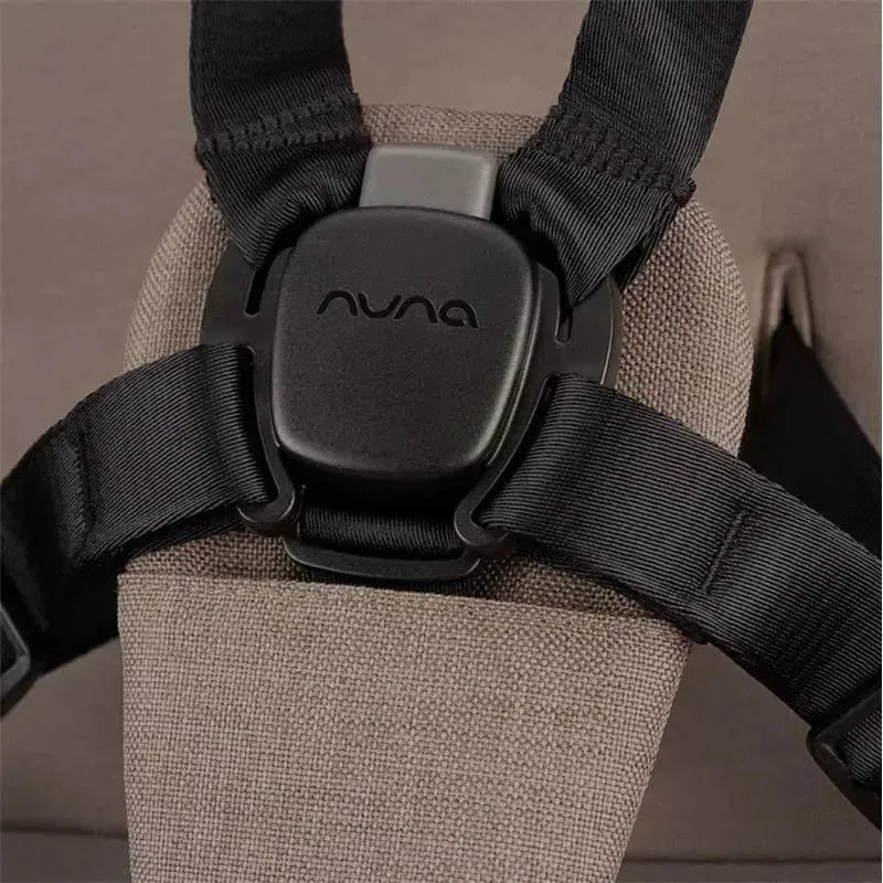 Close-up of the Nuna SWIV™ Stroller chest harness, featuring a black buckle and adjustable straps on a beige seat.