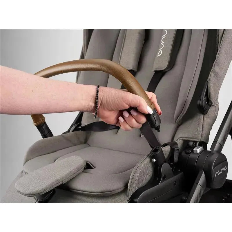 Hand grasping the brown handle of a Nuna SWIV™ stroller with a gray seat, showcasing its adjustable features.