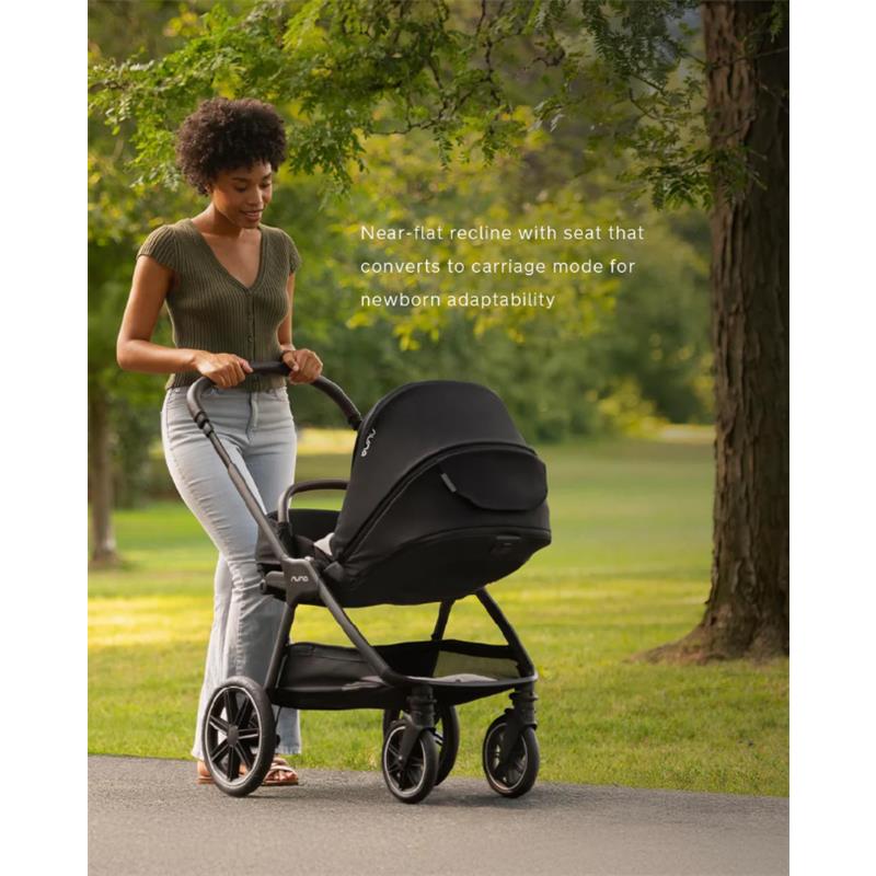 A woman pushes a Nuna Triv Lx stroller with a Pipa Urbn car seat in a park, showcasing its near-flat recline feature.