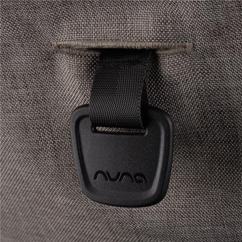 Close-up of the Nuna logo on a black buckle strap attached to gray fabric, part of the Nuna Trvl 360 Compact Stroller.