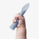 Soft-tip silicone training spoon for baby-led weaning, grasped by a small hand. Color: light blue.