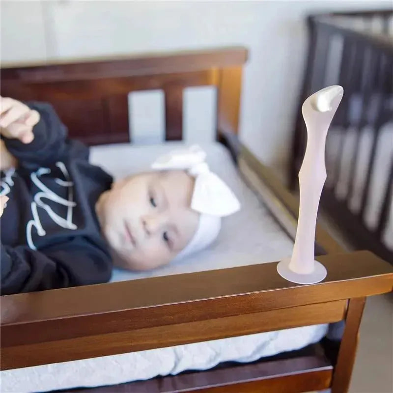 Diaper rash cream applicator with suction base positioned on a crib, while a baby lays nearby.