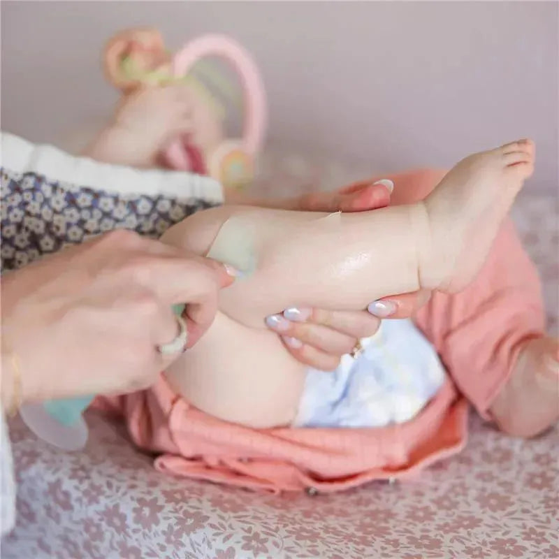 Diaper rash cream applicator being used on a baby’s leg, with the product visible and a suction base feature.