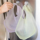 Lilac and yellow silicone waterproof baby bibs hanging on suction hooks, showcasing their flexible design for easy cleaning.