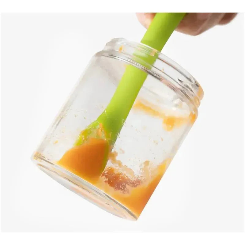 Green baby feeding spoon stirring orange puree in a glass jar, demonstrating use for feeding infants.