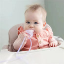 Baby seated in a high chair, holding a silicone strap in lemon color, partially in mouth, wearing a pink buttoned outfit.