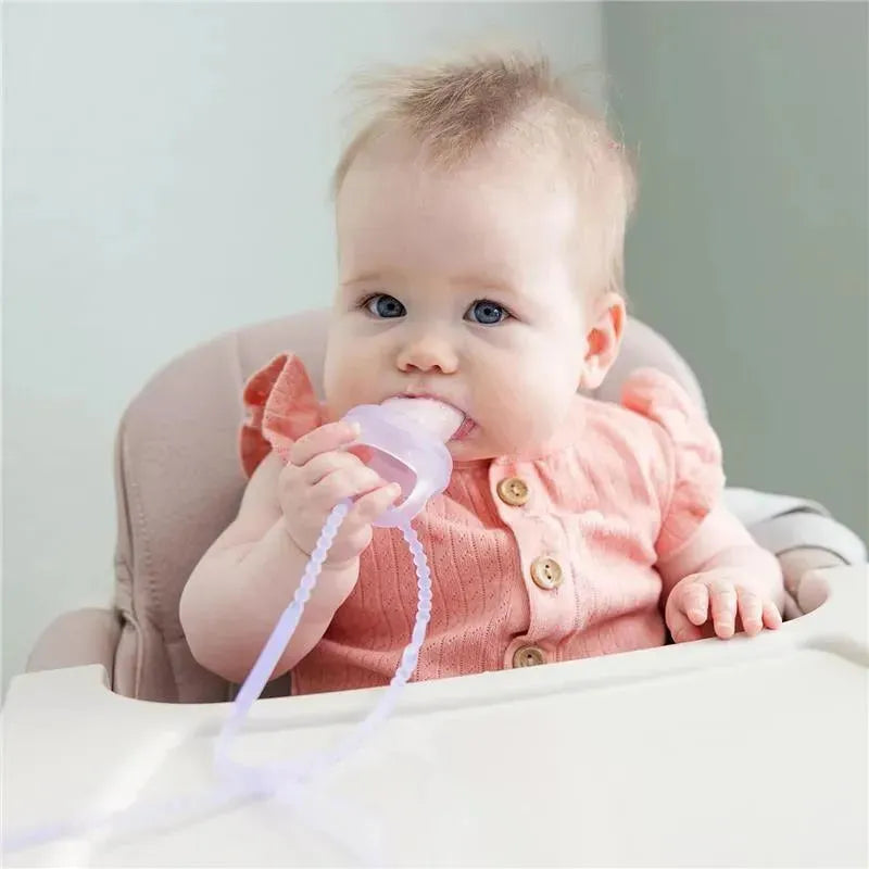 Infant with blue eyes holding a pink silicone pacifier with straps, sitting in a high chair.