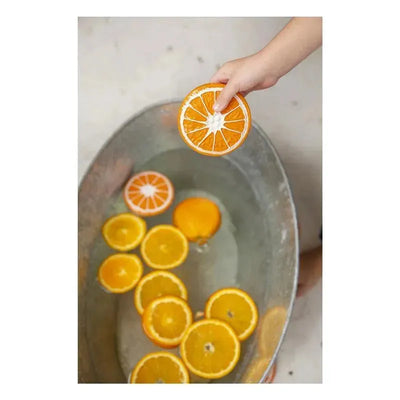 Chewable toy of a clementine orange held above a metal basin filled with water and floating orange slices.