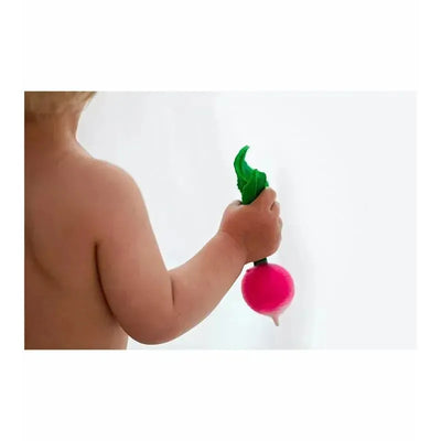 A child’s hand holds a pink chewable toy shaped like a radish with green leaves, designed for teething.