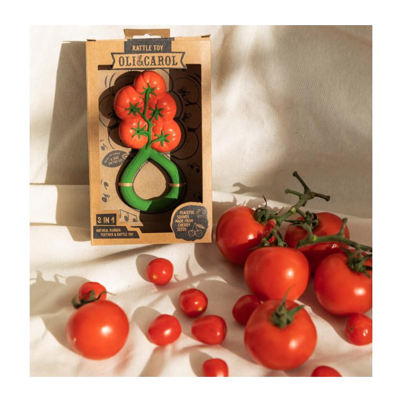 Oli & Carol Tomato Rattle Toy displayed in packaging, surrounded by fresh tomatoes, emphasizing its 2-in-1 design.