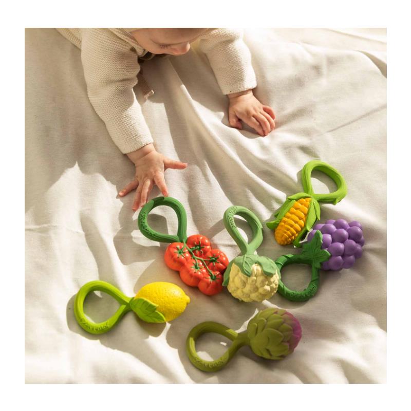 Colorful Oli & Carol rattle toys shaped like fruits and vegetables, with a baby reaching for them on a soft surface.