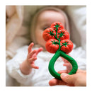 Oli & Carol tomato-shaped rattle toy held in a hand, with a baby reaching out in the background.
