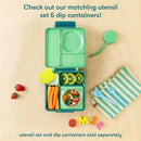 Lime and meadow green OmieBox lunchbox with compartments holding strawberries, carrots, kiwi, and a dip container on a wooden table.