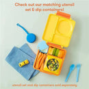 A blue and yellow OmieBox lunch container with compartments, containing fruit, veggies, and salad, beside utensils and a toy car.