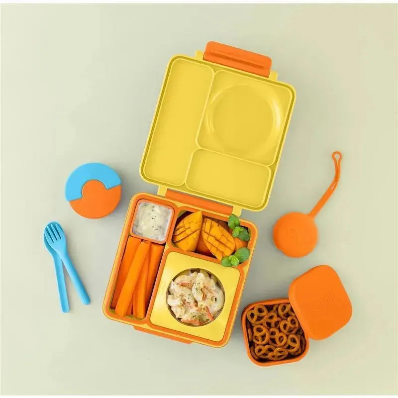 Orange OmieBox container with yellow compartments, carrot sticks, mango slices, a small container of dip, and pretzel snacks.