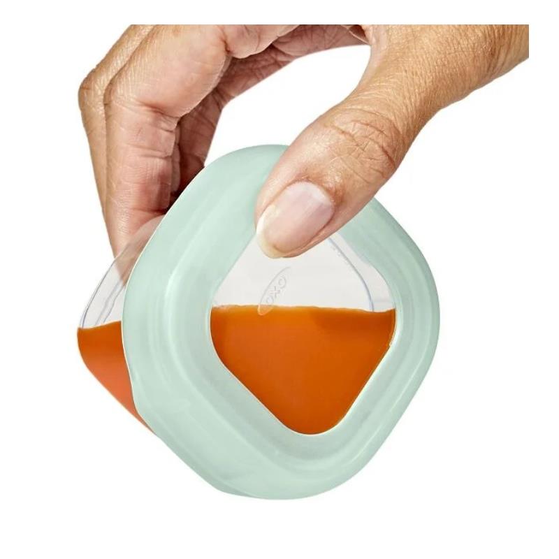 Oxo Tot 12 Pc Baby Blocks set with a hand holding a container filled with orange food.