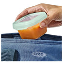 Hand holding an Oxo Tot food storage container filled with orange baby food, placing it into a blue bag.