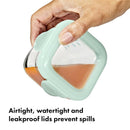 Oxo Tot 4 oz glass baby food storage container held in hand, featuring an airtight, watertight, and leakproof lid.