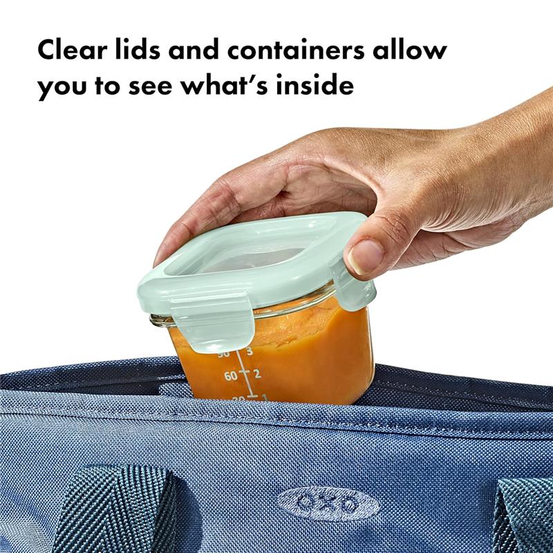 Clear glass baby food storage container with a light green lid; hand placing it into a blue bag.