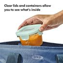 Clear glass baby food storage container with a light green lid; hand placing it into a blue bag.
