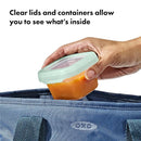 Clear 4 oz Oxo - Tot baby food storage container with a light green lid, being placed into a blue bag.