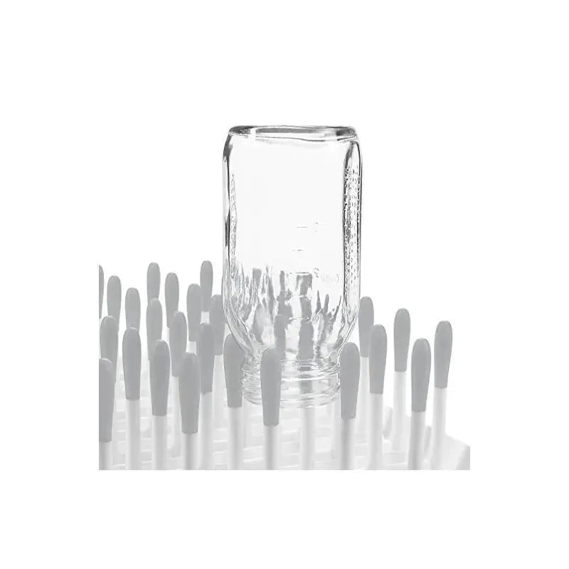 Clear glass bottle displayed on an OXO Tot Bottle Drying Rack, with white drying pegs surrounding it.