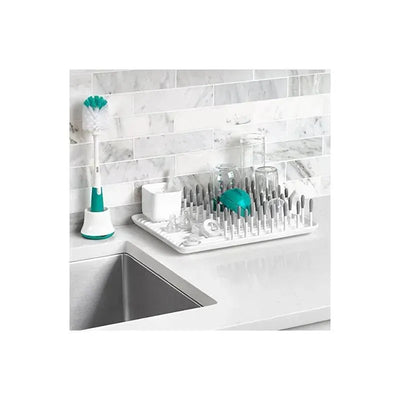 OXO Tot Bottle Drying Rack in gray with multiple prongs, bottles, and a bottle brush on a kitchen countertop.