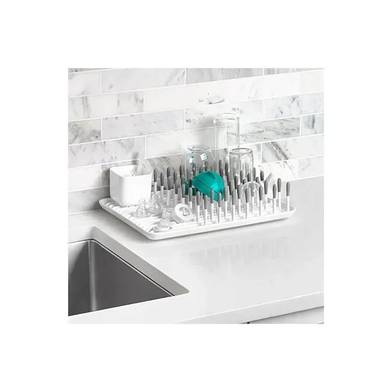 OXO Tot Bottle Drying Rack in gray with multiple drying pegs, holding baby bottles, glassware, and accessories on a countertop.