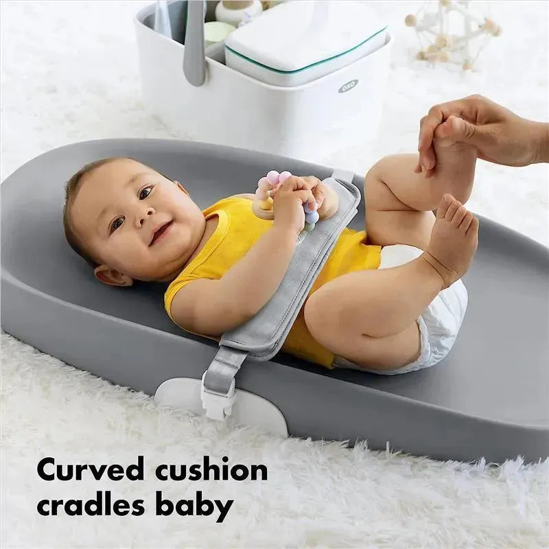 Curved OXO Tot Changing Pad with a baby wearing a yellow shirt, playing with a toy while being cradled and supported.